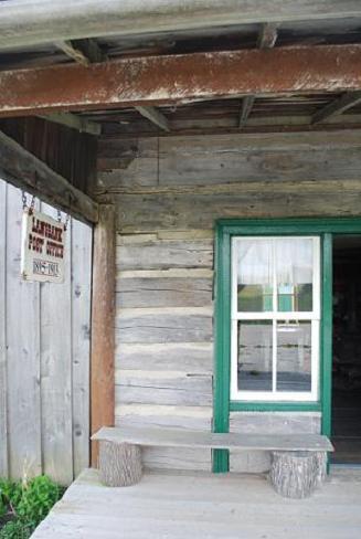 Post Office's front entrance, surrounded by original log; board and batten siding visible on left; Photographs taken by Dana Johnson, May 4th, 2010, with permission of  the Oil Museum of Canada