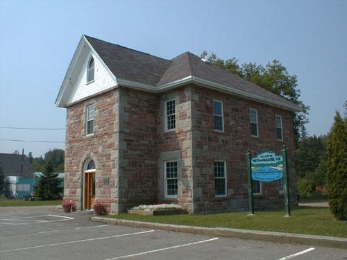 This corner view of the building presents the front projection around the central main entrance with a medium pitch roof and a front gable.; PNB 2004