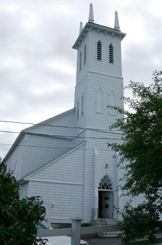 Image illustrates the wood construction with shingled exterior walls as well as the placement of decorative buttresses to the base of the tower and the embattlement and pinnacles at the top of the tower.; PNB 2004