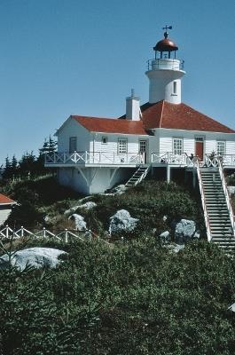General view of the lighthouse cylindrical tower, clad with painted metal panels, rising out of the wooden square building; Agence Parcs Canada | Parks Canada Agency, Jean-François Bergeron.