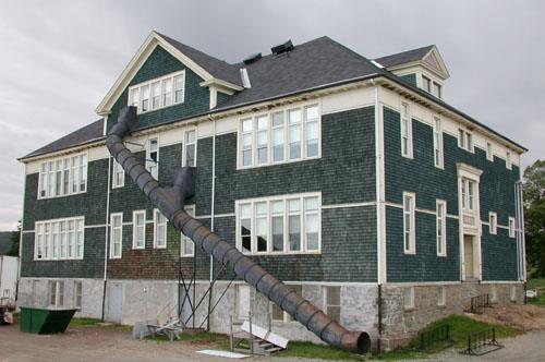 This corner view of the building illustrates the cut stone foundation and the stained wood shingles punctuated by wood trim window surrounds and corner boards.; PNB 2005