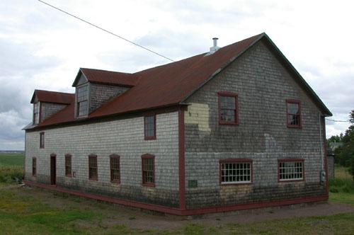 Corner view of the building illustrates the medium-pitched gable roof, slight roof overhangs of simple design, and gabled dormers typical of period small-scale industrial and farm buildings. ; PNB 2004