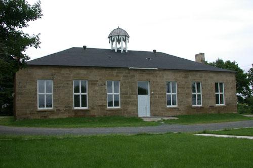 This image illustrates the symmetrical front façade of the rectangular sandstone building surmounted in the centre by a cupola.; PNB 2005