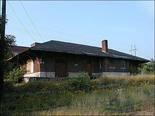 This image presents the building’s hipped roof with black asphalt shingles that has a wide overhang supported by decorative brackets resting on granite supports attached to the brick walls.; PNB 2005