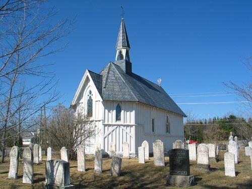 This image presents the context of the building surrounded by cemetery stones nestled in a churchyard in what still can be considered a rural community setting.; PNB 2005
