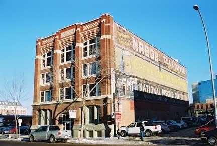This image illustrates the front, west-facing brick-clad facade of the HV Shaw Building showing the elaborate Chicago School-influenced decorations and the south elevation with its painted signs.; City of Edmonton, 2004