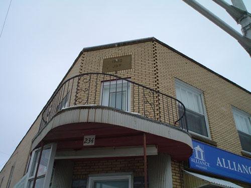 This image shows the small balcony overhanging the angled entrance.; Village of Saint Quentin