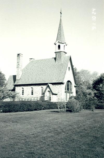 Side view of the Memorial Chapel, showing the simple steeple set on the roof just behind the main entrance, and the steeply pitched copper roof with bell-cast eaves, 1991.; Canadian Parks Service, Atlantic Regional Office/ Service canadien des parcs, Bureau régional de l'Atlantique, 1991.