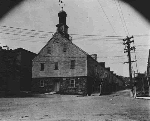 HMC Dockyard Clock in its original location at the Hauser Stores, Halifax Dockyards, Halifax, Nova Scotia, 1941. The "x" motif can been seen in a railing surrounding the base of the tower.; HMC Dockyard, base photographic section, CFB Halifax, Halifax, NS, 1941.