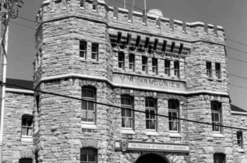 Façade of the Armoury, showing the prominent three-storey projecting frontispiece, consisting of a troop door and two flanking stair towers, 1989.; Parks Canada | Parcs Canada, J. Adell, 1989.