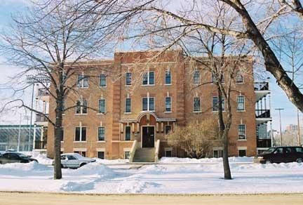 This image illustrates the overall form and massing of the Ross Flats Apartment, in its prominent river valley location. The facades are constructed of brick and the end balconies are from wood. ; City of Edmonton, 2004