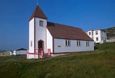 General view of Battle Harbour Historic District, St. James the Apostle Anglican Church with its rectangular, gable-roofed massing, clapboarding, two-stories and pyramidal tower, 2003.; Parks Canada Agency/Agence Parcs Canada, J. McQuarrie, 2003.