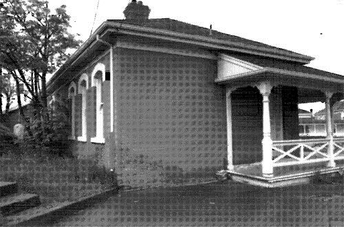 Corner view of the northeast elevation of Building 29, showing the the verandah with decorative woodwork and railing on the main elevation, 1989.; Parks Canada Agency/Agence Parcs Canada, I. Doull, 1989.