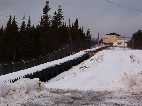 Exterior view of the wooden flume constructed by Bernard J. Miller (1877-1949).  This flume was the first of its kind built in Newfoundland. The substation can be seen in the upper right corner. Photo taken January 2006.; HFNL/ Lara Maynard 2006.