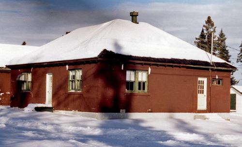 General view of Building 8, showing the one-storey, hip-roofed construction of brown painted smooth stucco on concrete blocks, 1996.; Canadian Forest Service / Service canadien des forêts, 1996.