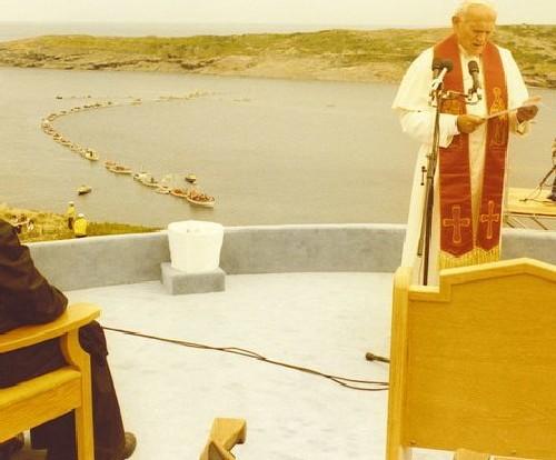 Pope John Paul II at the Blessing of the Fleet and Homily Site, Flatrock, with boats in the harbour in the background, on 1984/09/12.; Courtesy Archives of the Roman Catholic Archdiocese, St. John's, NL.