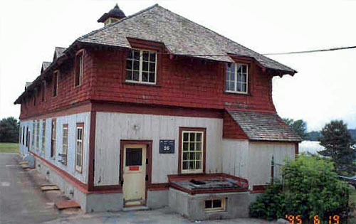 Corner view of the east elevation of the Service Building showing the board-and-batten siding on the ground floor and the wood shingled side walls on the second storey with a slight outward flare, 1995.; Parks Canada Agency / Agence Parcs Canada, C. Zacconi, 1995.
