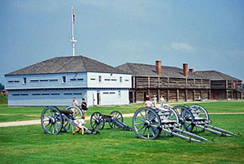 Panoramic view of Blockhouse 1 emphasizing its simple design and materials that harmonize with the nearby cottage and adjacent blockhouses and other buildings within the military setting, 1994.; Parks Canada Agency / Agence Parcs Canada, B. Morin, 1994.