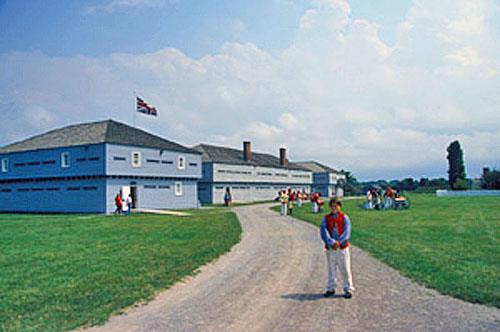 Panoramic view of Blockhouse 3 emphasizing its simple design and materials that harmonize with the adjacent blockhouses, the nearby cottage and the other buildings within the military setting, 2003.; Parks Canada Agency / Agence Parcs Canada, B. Morin, 2003.