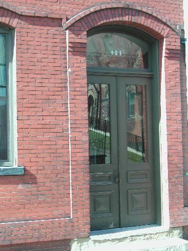 This photograph shows the wooden door and transom window under the arched entranceway, 2004; City of Saint John