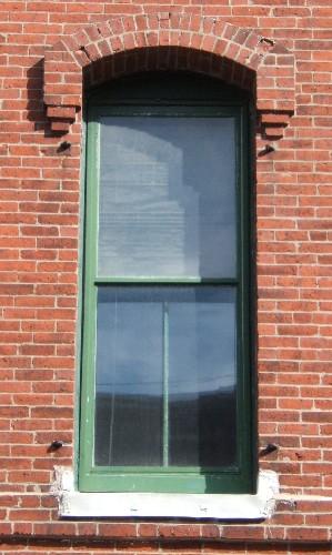 This image provides a view of a segmented arch opening encasing a 2/2, vertical sliding wood window below a brick hood mold, 2005.
; City of Saint John