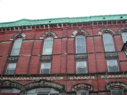 This photograph shows the metal cornice with brackets and the Roman arch and square windows on the top two floors, 2004; City of Saint John
