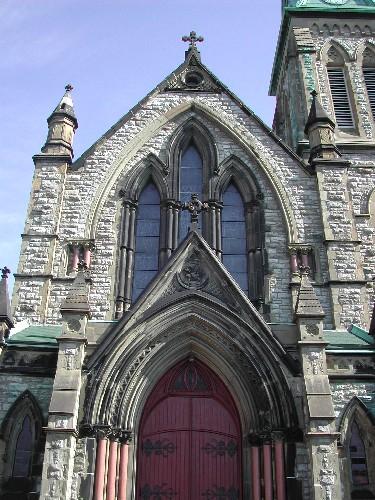 This photograph shows the ornate detailing, the large gothic window, pinnacles, supporting corinthian columns, gothic arched door and entranceway, crosses, and flag bearing lamb insignia, 2004; City of Saint John