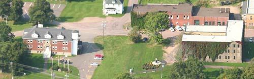 Aerial view of a portion of Butte à Pétard: Municipal Building to the left (south side); former Littles Sisters Convent, site of the first collège built in Memramcook.; Memramcook Valley Historical Society