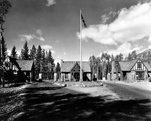 View of the East Gate Registration Buildings, with Building 2 in the middle, showing the manner in which the East Gate Registration Buildings reinforce the picturesque character of their mountain park setting, 1985.; Parks Canada Agency / Agence Parcs Canada, 1985.