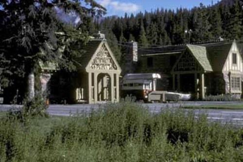 Side view of Building 3, showing the gabled roof, with one stone chimney and the cedar-shingles laid in staggered lines to give a random roof pattern, 1985.; Parks Canada | Parcs Canada, 1985.