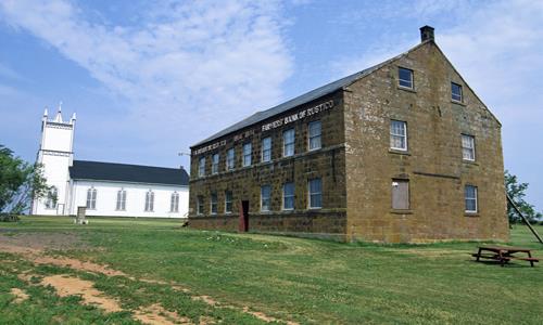 General view of Farmers' Bank of Rustico showing the building’s location amongst a cluster of buildings near the church of St. Augustine.; Parks Canada Agency / Agence Parcs Canada.