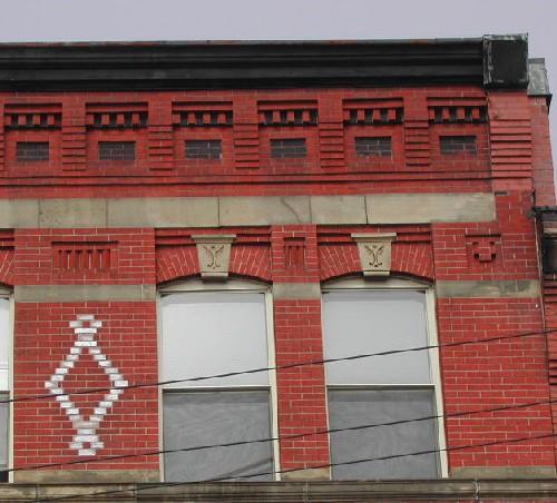 This photograph shows the roof-line cornice, corbel bands, sandstone work, and upper storey segmented arch openings, 2005; City of Saint John