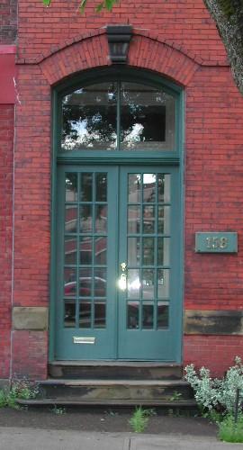 This image provides a view of the paired wood doors with glass panels below the segmented arch transom window, 2005.; City of Saint John