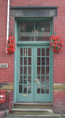 This image provides a view of the paired wood doors with glass panels below the two paned, rectangular transom window and the sandstone lintel, 2005.; City of Saint John