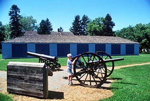 General view of Butler's Barracks showing the Gunshed in its rectangular, single-storey massing under low, hipped roof, and main façade with seven bays of double shed doors, 1993.; Parks Canada Agency / Agence Parcs Canada, B. Morin, 1993.