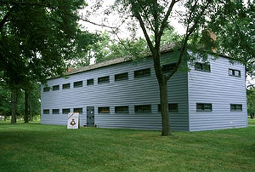 General view of Butler's Barracks showing the Soldiers’ Barracks in its rectangular, two-storey massing under low, hipped roof, brick wall infill, and regularly placed, horizontally shaped windows, 1994.; Parks Canada Agency / Agence Parcs Canada, B. Morin, 1994.