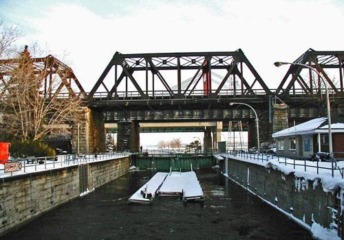General view of Sainte-Anne-de-Bellevue Canal, showing the entrance walls above and below the lock, and the stone masonry coping of the lock walls, 2003.; Parks Canada Agency / Agence Parcs Canada, 2003.