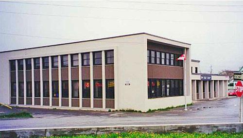 Corner view of the Government of Canada Building showing the flat, cement surfaces without decorative detailing, and the simplicity and abstraction of all components, 1999.; Travaux publics et Services gouvernementaux Canada / Public Works and Government Services Canada, 1999.