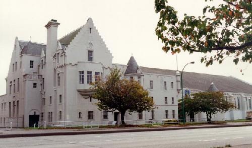Corner view of the Seaforth Armoury, showing the roofs, the two circular towers with conical roofs, the massive stepped buttresses, and the large stepped chimney.; Department of National Defence / Ministère de la Défense nationale