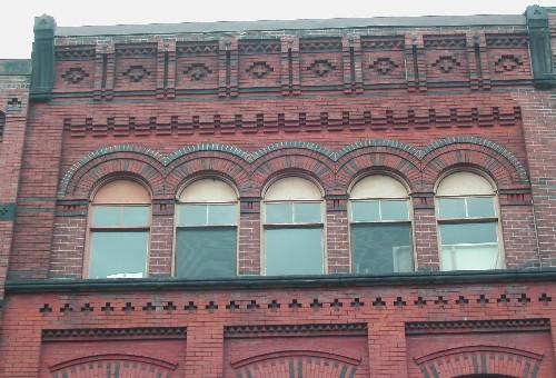 This photograph shows the bracketed cornice, the detailed brick design and Roman arch windows, 2005 ; City of Saint John