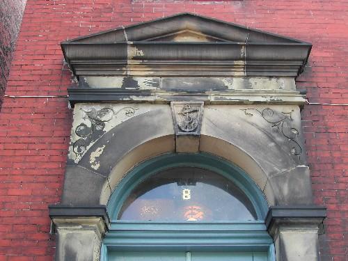 This photograph shows the pediment entablature and transom window above the entrance and the anchor insignia in the keystone, 2005.; City of Saint John