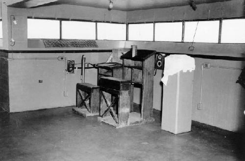 Interior view of the Battery Command Post, showing the Battery Commander's desk and depression rangefinder pedestal, ca. 1945.; Department of National Defence / Ministère de la Défense nationale, 1945.