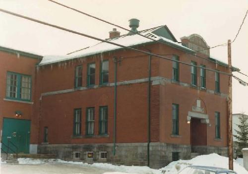 Corner view of the Armoury, showing the exterior executed in red brick and the stone-trimmed pediment on the principal façade, 1987.; Department of National Defence / Ministère de la Défense nationale, 1987.
