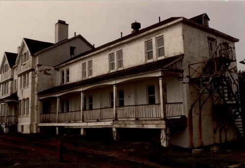 Corner view of Building 14, showing the simple, principal façade that features gables with false half timbering, a front porch, long verandahs and exterior fire escapes.; Agence Parcs Canada / Parks Canada Agency.