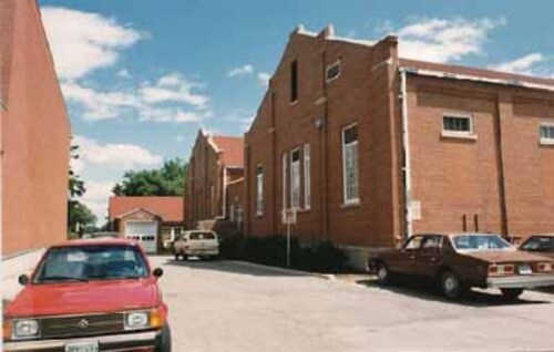 A view of the north façade of the RCMP Gymnasium and Pool Building, showing the red brick construction and the symmetrical window arrangement, 1986.; Royal Canadian Mounted Police / Gendarmerie royale du Canada, 1986.