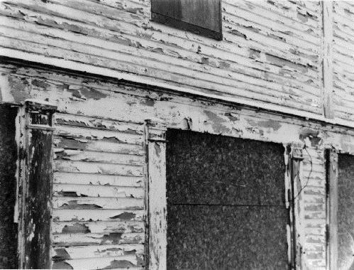 Detail view of the Ryan Retail Store, showing the boarded-up windows on the façade of the building, 1991.; Agence Parcs Canada / Parks Canada Agency, 1991.
